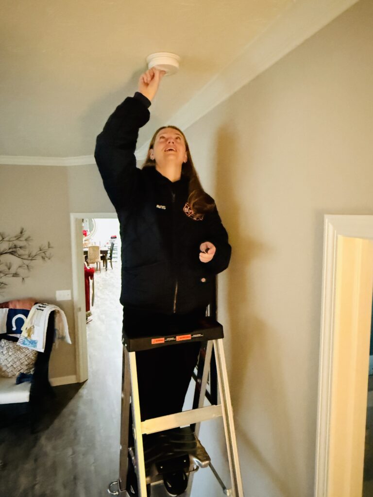 woman on ladder changing smoke alarm